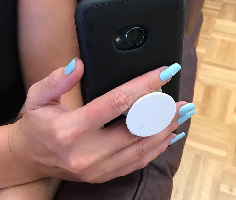 A picture of a phone case with a special button grip. The grip is allowing a hand to grasp it better and stop it from falling.